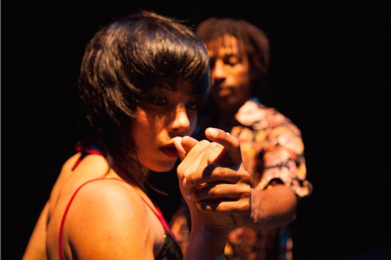 A close up of a woman extending her hand in front of her face with a man watching in the background